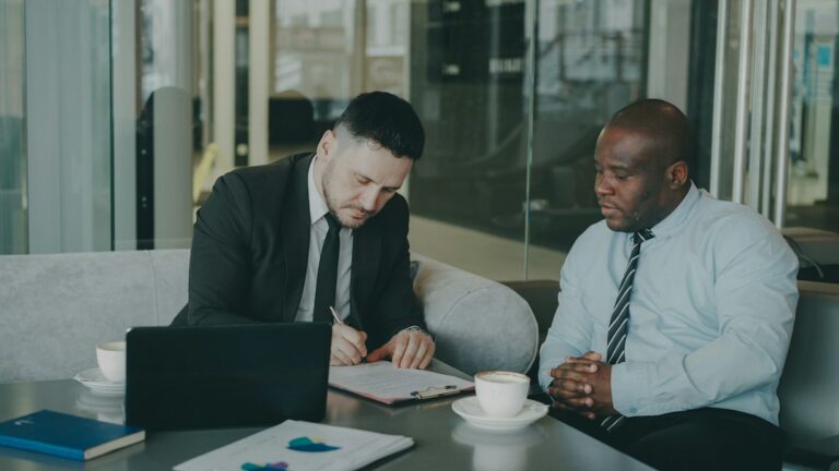 Two business partners reviewing and signing a contract at a table with a laptop