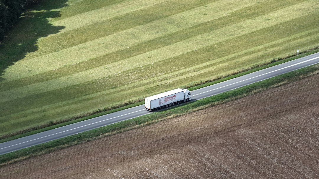 White semi truck driving on a rural road through open fields