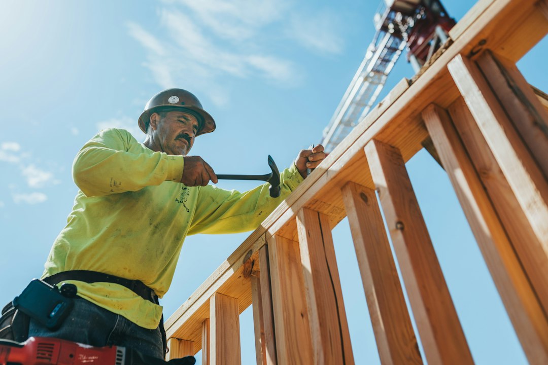 Subcontractor in a hard hat and safety gear framing a wooden structure on a construction project